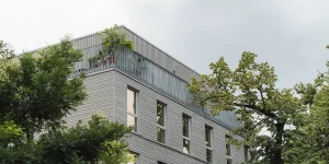 Mehrfamilienhaus mit grauer Holzfassade und Staffelgeschoss mit umlaufendem Balkon
